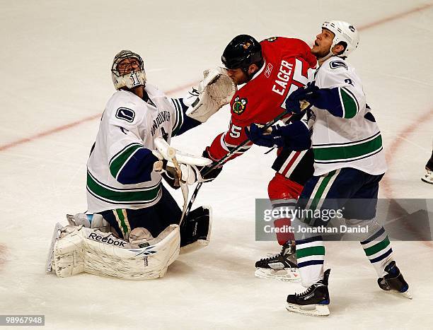 Roberto Luongo and Kevin Bieksa of the Vancouver Canucks look in the air for the puck as Ben Eager of the Chicago Blackhawks slips between them in...