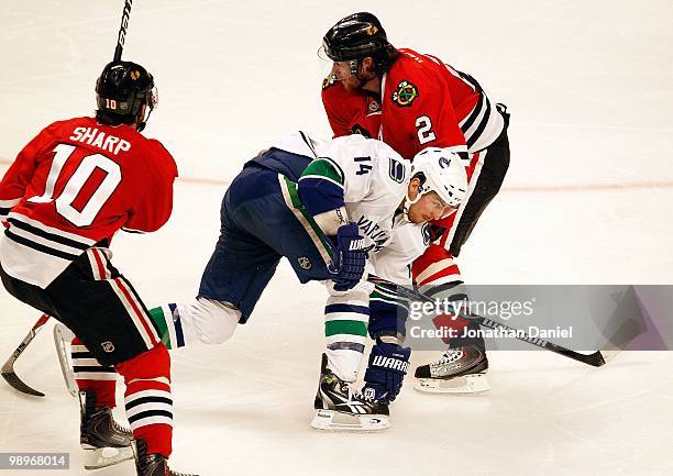 Alexandre Burrows of the Vancouver Canucks slips between Patrick Sharp and Duncan Keith of the Chicago Blackhawks in Game Five of the Western...