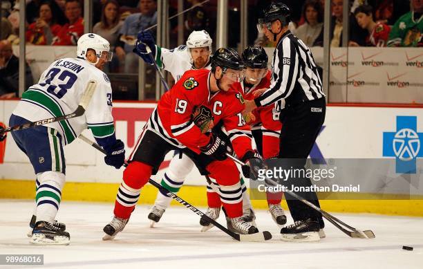Jonathan Toews of the Chicago Blackhawks tries to control the puck followed by teammate Patrick Kane and Henrik Sedin and Daniel Sedin of the...