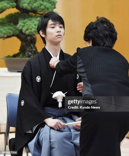 Japanese star figure skater Yuzuru Hanyu, wearing a special type of "hakama" skirt originated in his hometown Sendai, has his kimono fixed while...