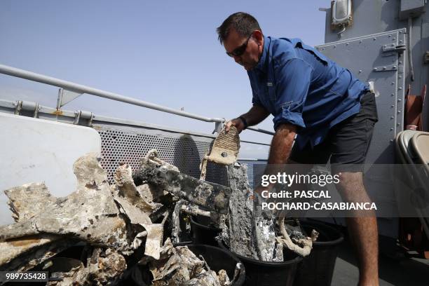 Staff member of the US agency the Defense POW/MIA Accounting Agency inspects fragments of a plane on the deck of the French FS Pluton M622 navy...