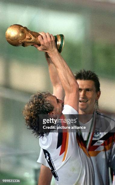 Overjoyed German player Rudi Voeller cheers and jubilates as he holds up the World Cup trophy while his teammate joins in and smiles after the 2002...
