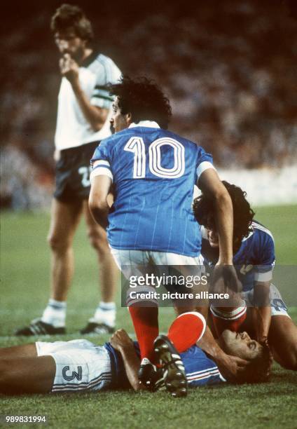 French defender Patrick Battiston lies unconscious on the pitch and is being looked after by his teammates Michel Platini and Didier Six after a...