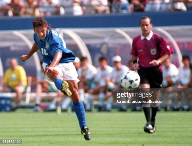 Italian forward Roberto Baggio throws his leg into the air and kicks the ball while French referee Joel Quiniou watches the scene during the 1994...