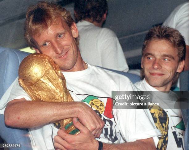 German defender Andreas Brehme holds the World Cup in his arms minutes before the German team bus is set to take off while his team-mate Thomas...