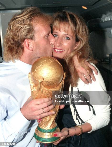 German defender Andreas Brehme holds the World Cup trophy in his hand while he kisses his wife Pilar on their return trip to Frankfurt Main after...