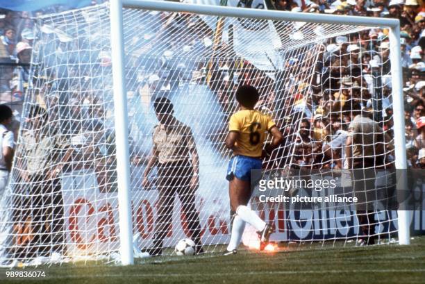 Brazilian midfielder Junior collects the ball from the Italian goal as Brazilian supporters throw burning fireworks on the pitch despite futile tries...