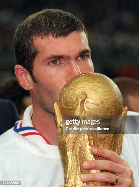 French midfielder and goalgetter Zinedine Zidane kisses the World Cup trophy which he holds in his hands after 1998 World Cup soccer game France...