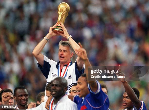 French soccer coach Aime Jacquet cheers and laughs with his players while he holds the World Cup trophy in his hands after the 1998 World Cup final...