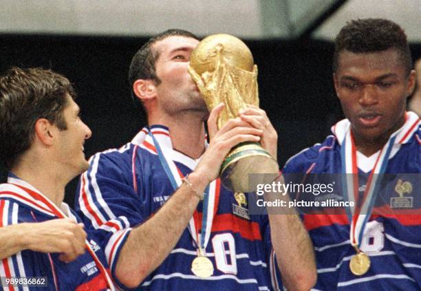 French players Bixente Lizarazu and Marcel Desailly watch midfield mastermind Zinedine Zidane kissing the World Cup trophy during the awards ceremony...