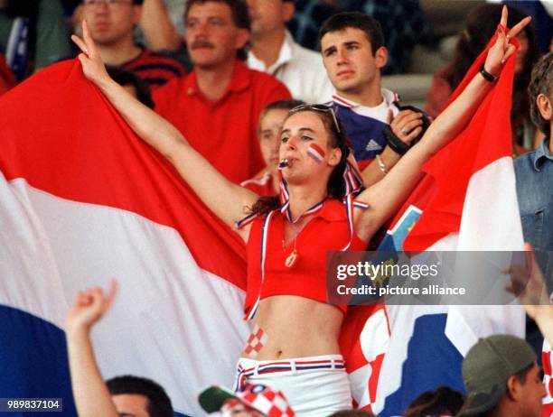 Young Croatian woman with a whistle in her mouth, holds the Croatian national flag as she raises her arms displaying the victory sign while she...