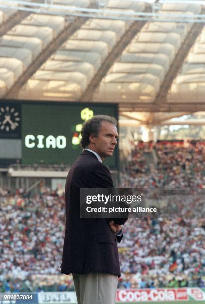 German head coach Franz Beckenbauer stands with folded arms on the side line of the pitch and watches with a serious expression on his face the 1990...
