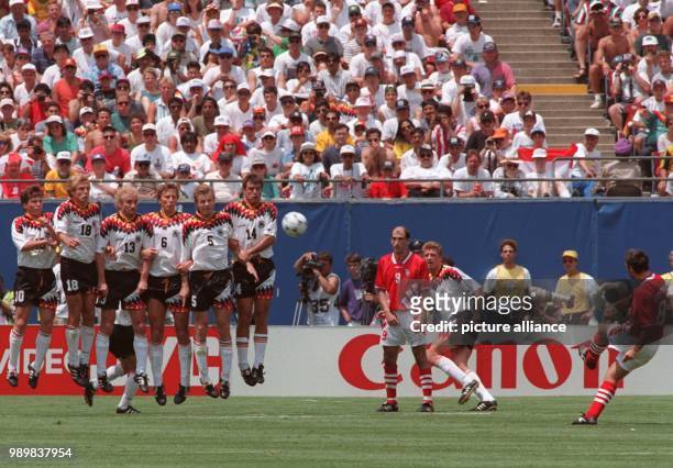 Bulgarian forward Hristo Stoichkov kicks the ball across the pitch with a free kick towards the wall formed by six German players who jump up in...