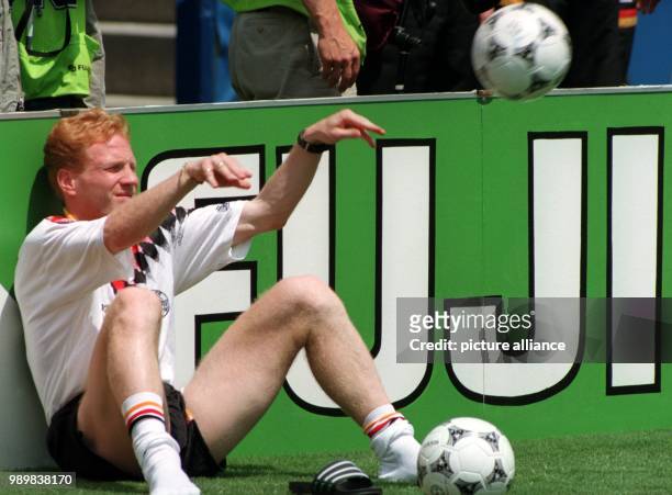 German midfielder Matthias Sammer sits behind the sideline of the pitch as a substitute and plays with a soccer ball while he watches the 1994 World...