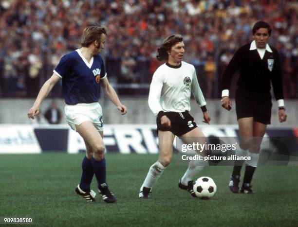 West German forward Juergen Grabowski has the ball while East German defender Siegmar Waetzlich runs next to him waiting for his chance and Uruguayan...