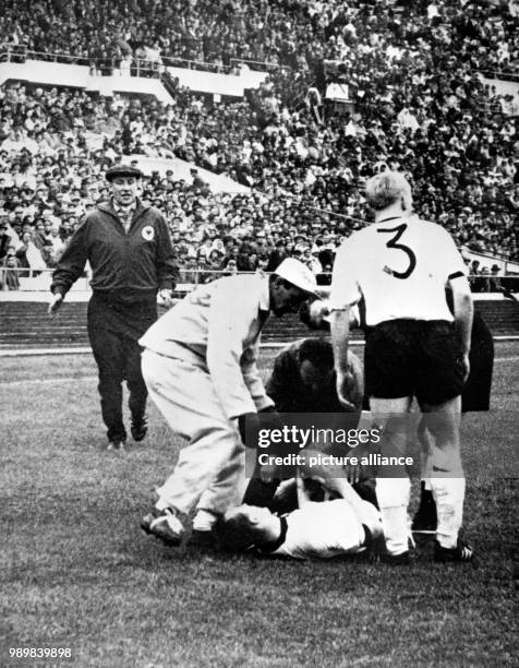 German defender Willi Schulz is lying on the ground injured after foulplay by Italian striker Omar Sivori and is being taken care of. Next to the...