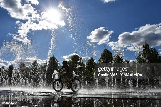 Youth rides a bike through a water fountain in a Gorky park in central Moscow on July 2, 2018.