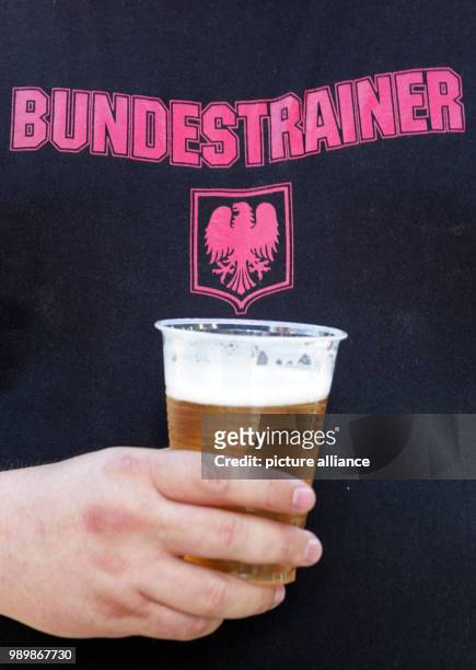 Ein Mann trägt am Dienstag auf der Fanmeile in Berlin eine T-Shirt mit der Aufschrift "Bundestrainer" und hält einen Becher mit Bier in der Hand....