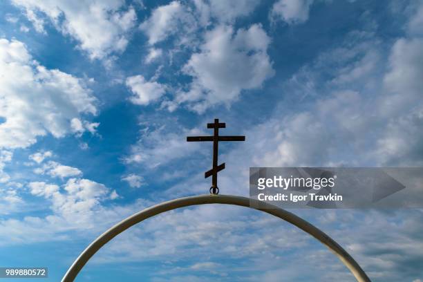 white semi-circular arch of iron pipe with dark orthodox cross on it against the blue sky with cloud - iron cross stock pictures, royalty-free photos & images