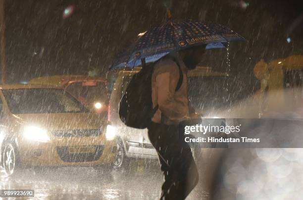 Man uses an umbrella to protect himself during sudden monsoon showers at Connaught Place area on July 2, 2018 in New Delhi, India. Heavy rain lashed...