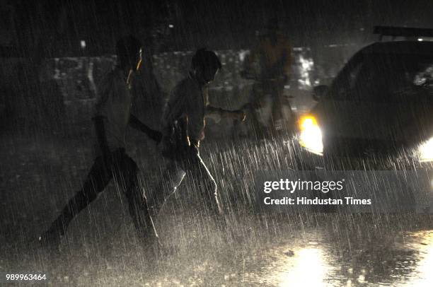 People cross a road during rainfall on July 2, 2018 in Noida, India. Heavy rain lashed parts of Delhi and the National Capital Region bringing relief...