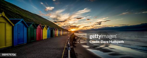brightly coloured beach huts by the water, whitby beach, yorkshire, england, uk. - whitby stock pictures, royalty-free photos & images