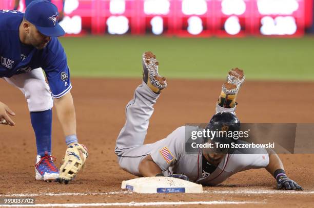 Jeimer Candelario of the Detroit Tigers slides back safely to first base on a pick-off attempt as Kendrys Morales of the Toronto Blue Jays tries to...