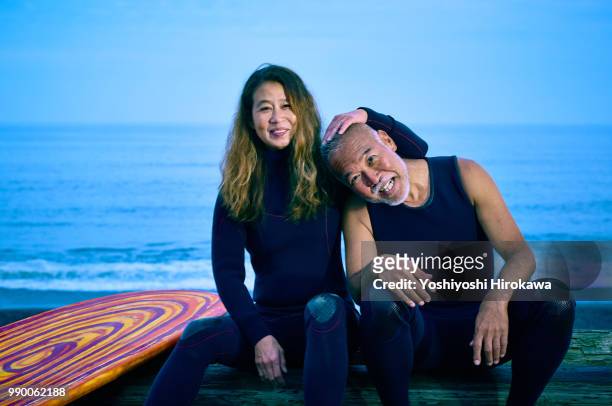 senior couple sit on the sea sand before surfing early in the morning next to surfboard - the japanese wife foto e immagini stock