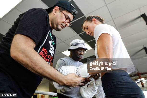 Manager George Ruiz and trainer Al Mitchell help take the gloves off boxer Mikaela Mayer as she wraps up her media workout at Azteca Gym on June 27,...