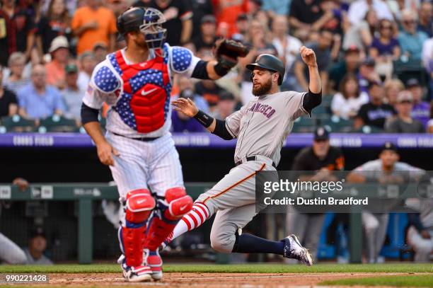 Brandon Belt of the San Francisco Giants slides to score as Chris Iannetta of the Colorado Rockies waits for the throw in the third inning of a game...