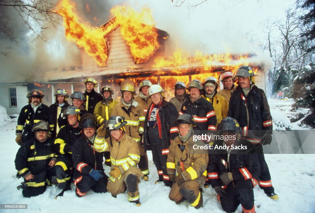 Group of firefighters posing in front of burning house, winter