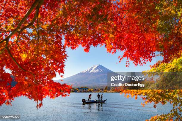 fuji mountain and fisherman boat with red maple leaves in autumn at kawaguchiko lake, japan - fujikawaguchiko stock-fotos und bilder