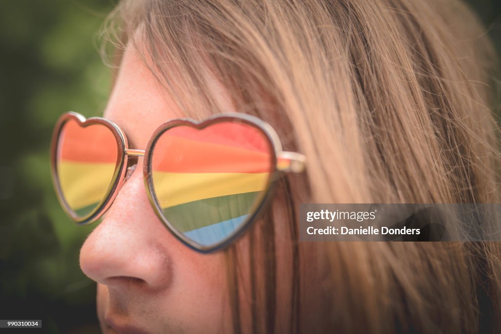 Reflection of rainbow pride flag in young person's heart-shaped glasses