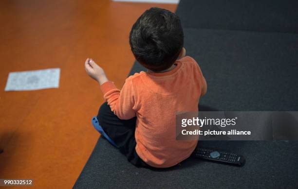Child sitting on a couch in front of a television at the emergency shelter for homeless people of the Diakonisches Werk Stadtmitte in Berlin,...