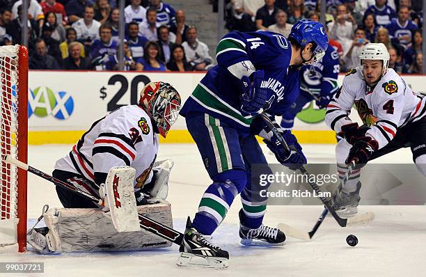 Alex Burrows of the Vancouver Canucks tries to control a bouncing puck while goalie Antti Niemi and Niklas Hjalmarsson of the Chicago Blackhawks look...