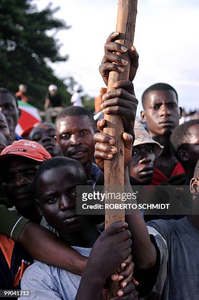Burundian men hold on to stick as they crowd the edge of a sports field during a political rally for the ruling party at a sports field in Bujumbura...