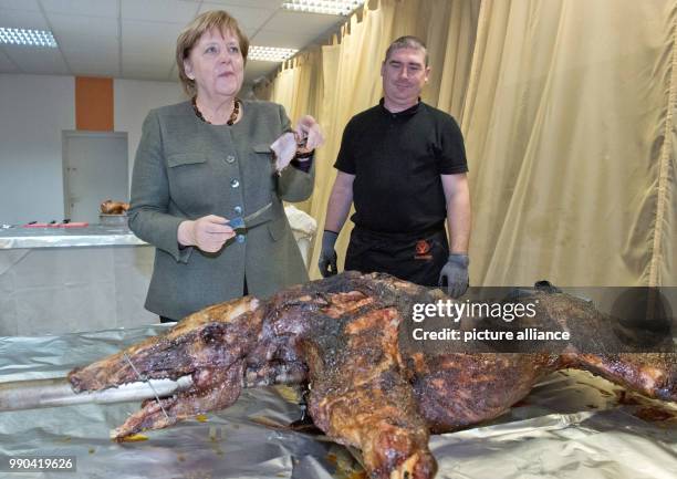 German Chancellor Angela Merkel stands next to butcher Andre Teuerung and waits for the first piece of roast wild boar during the New Year's...