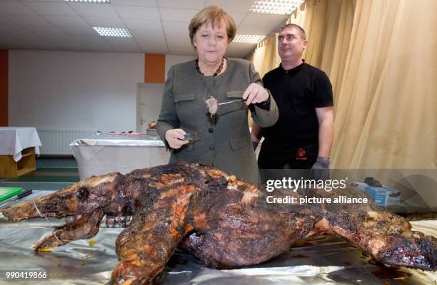 German Chancellor Angela Merkel stands next to butcher Andre Teuerung and waits for the first piece of roast wild boar during the New Year's...