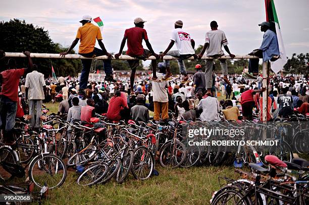 Burundian cyclists sit atop a soccer goal post above a line of parked bicycles during a political rally for the ruling party at a sports field in...