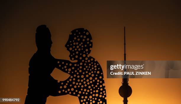 The tv-tower and the "Molecule Man" art work by US sculptor Jonathan Borofsky silhouette against the sky as sun sets in Berlin on July 2, 2018. /...