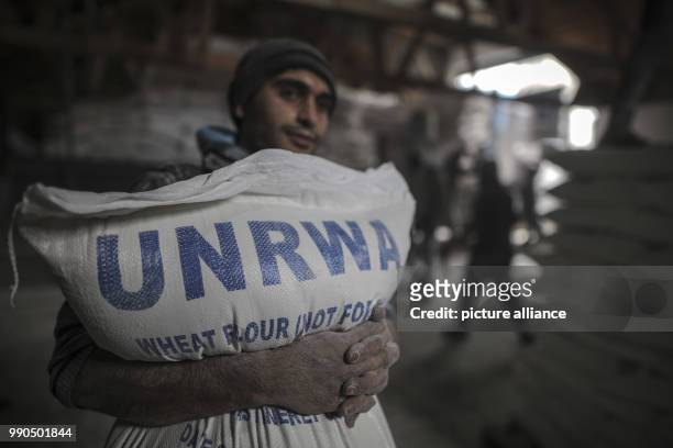 Palestinian man carries sacks of flour at a United Nations food distribution center in Al-Shati refugee camp in Gaza City, Gaza, 15 January 2018. US...