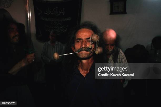 Dervish in trance, during remembrance ceremony of Kasnazani sect which with three skewers pushed into his cheeks and his jaw. In the background...