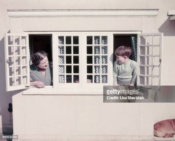 The Queen Mother and Prince Charles at a window in the little Welsh house at the Royal Lodge in Windsor in England on 7 April 1954.