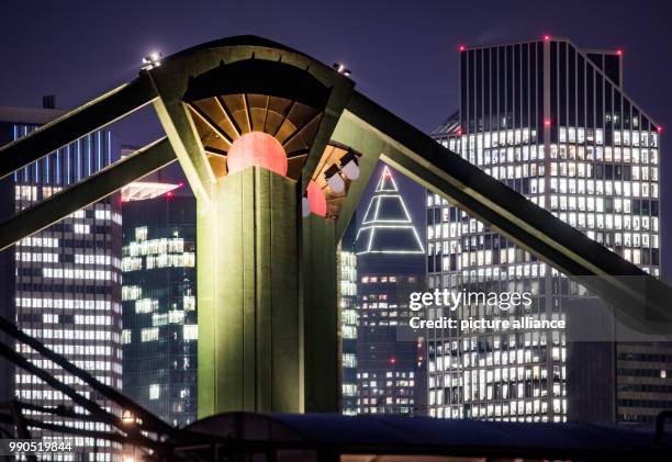 The concrete support of the Ignatz-Bubis-Bridge stand in front of the illuminated office buildings of the bank skyline during night time in Frankfurt...