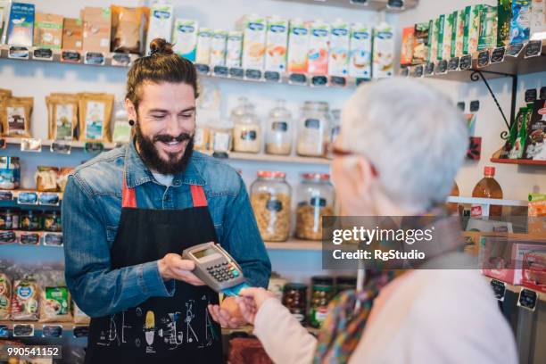 happy sales man handing credit card reader to senior woman - pin entry stock pictures, royalty-free photos & images