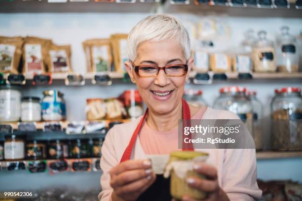 happy mature woman labeling food jar at the store - labeling stock pictures, royalty-free photos & images