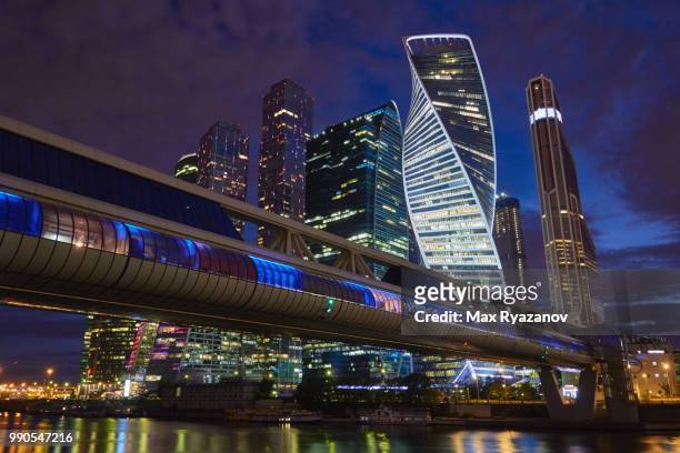 dense skyscrapers near the river at dusk and a pedestrian bridge in the foreground - moscow international business center stock pictures, royalty-free photos & images