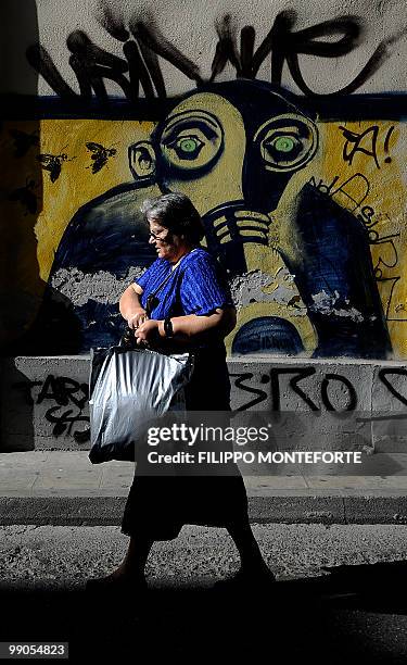 An old woman walk past a grafiti depicting a person with the teargas-mask in central Athens on May 12, 2010. Greece on Wednesday was to receive a...