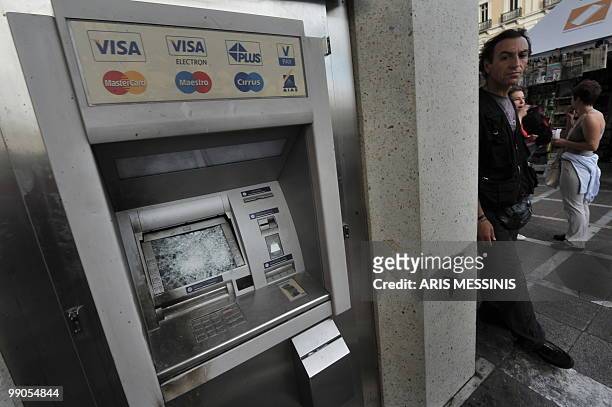Man sit stands next to a smashed cash machine during a demonstration against government's austerity measures in central Athens on May 12, 2010....
