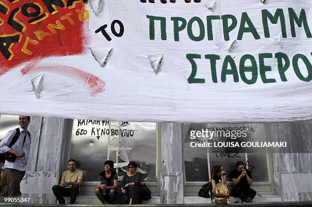 People sit behind a banner by a protected shop windows in Athens during a protest on May 12, 2010. Greece was to receive a first dose of 5.5 billion...